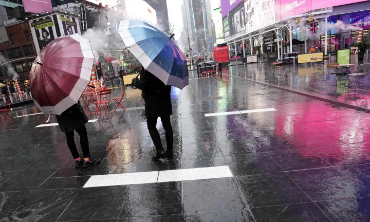 People with an umbrella walk through the rain at Time Square , in New York City October 16, 2020. - The US budget deficit surged 218 percent to a record $3.1 trillion in the fiscal year ended September 30 due to a massive increase in spending to help the economy weather the coronavirus pandemic, the government announced October 16, 2020. (Photo by TIMOTHY A. CLARY / AFP)