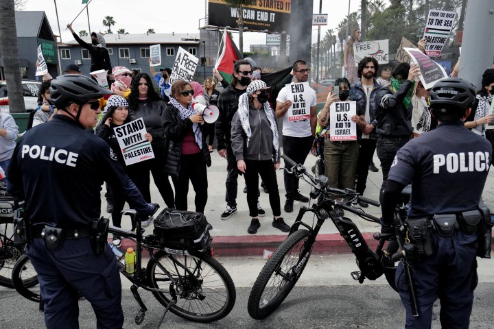 People hold signs next to law enforcement officers during a protest near the perimeter of the 96th Academy Awards, amid the ongoing conflict between Israel and the Palestinian Islamist group Hamas, in Los Angeles, California, U.S., March 10, 2024. REUTERS/Carlin Stiehl